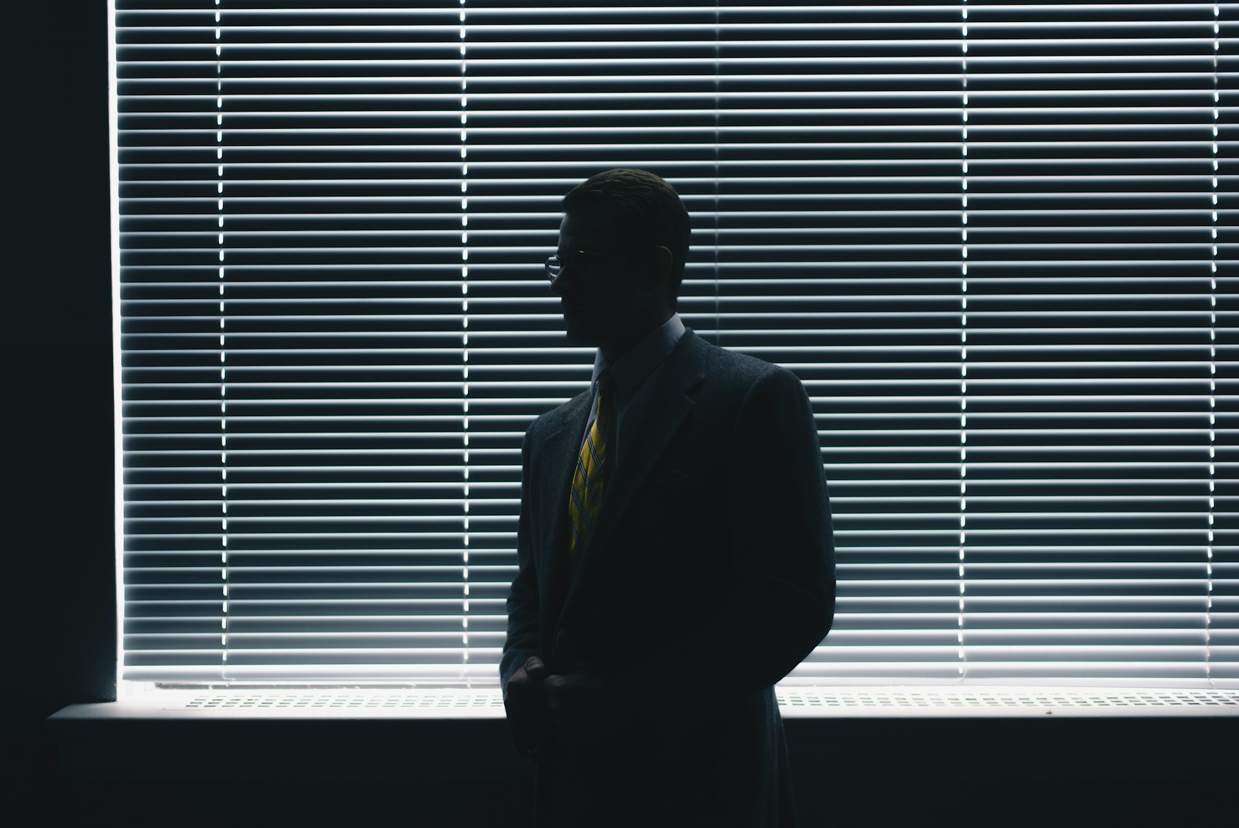 Investigator silhouetted against window blinds in a Denver office, evoking discreet professional surveillance